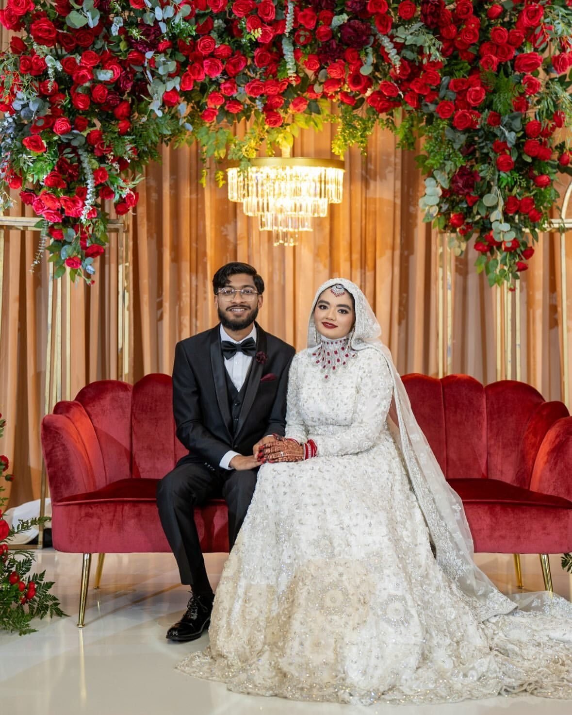 Couple seated at their reception stage with red florals